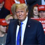 Inflation Fears Loom as Trump Pressures Fed Person at a rally with Make America Great Again signs.