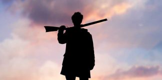 Silhouette of a person holding a rifle against a colorful sunset sky
