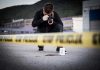 ICE Agent Shoots Woman During MASSIVE Federal Operation Crime scene photographer behind police tape with evidence marker.