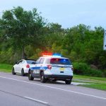 Police car with flashing lights pulling over a white vehicle beside a speed limit sign